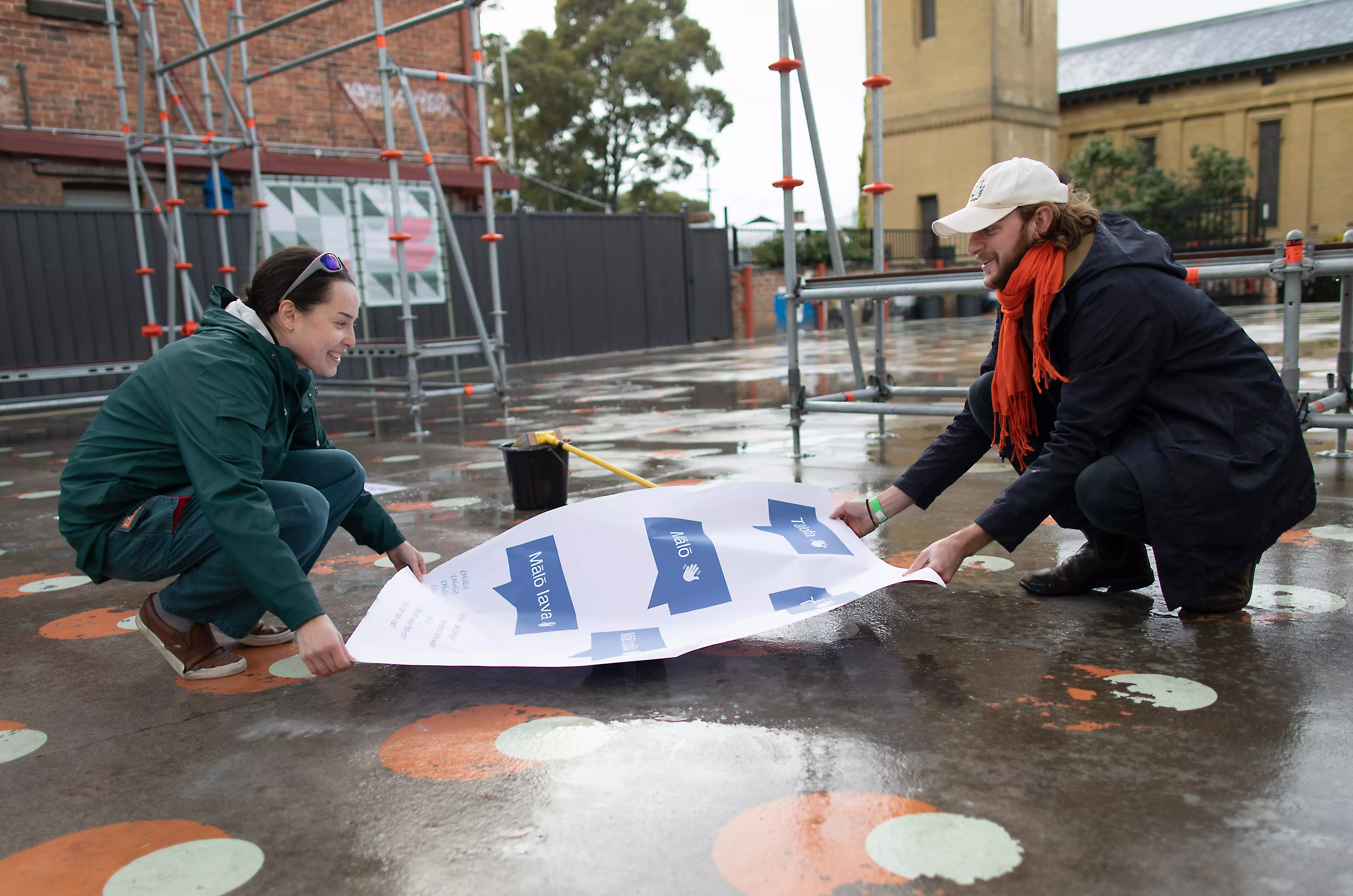 Two people placing installing a poster on the ground while smiling.