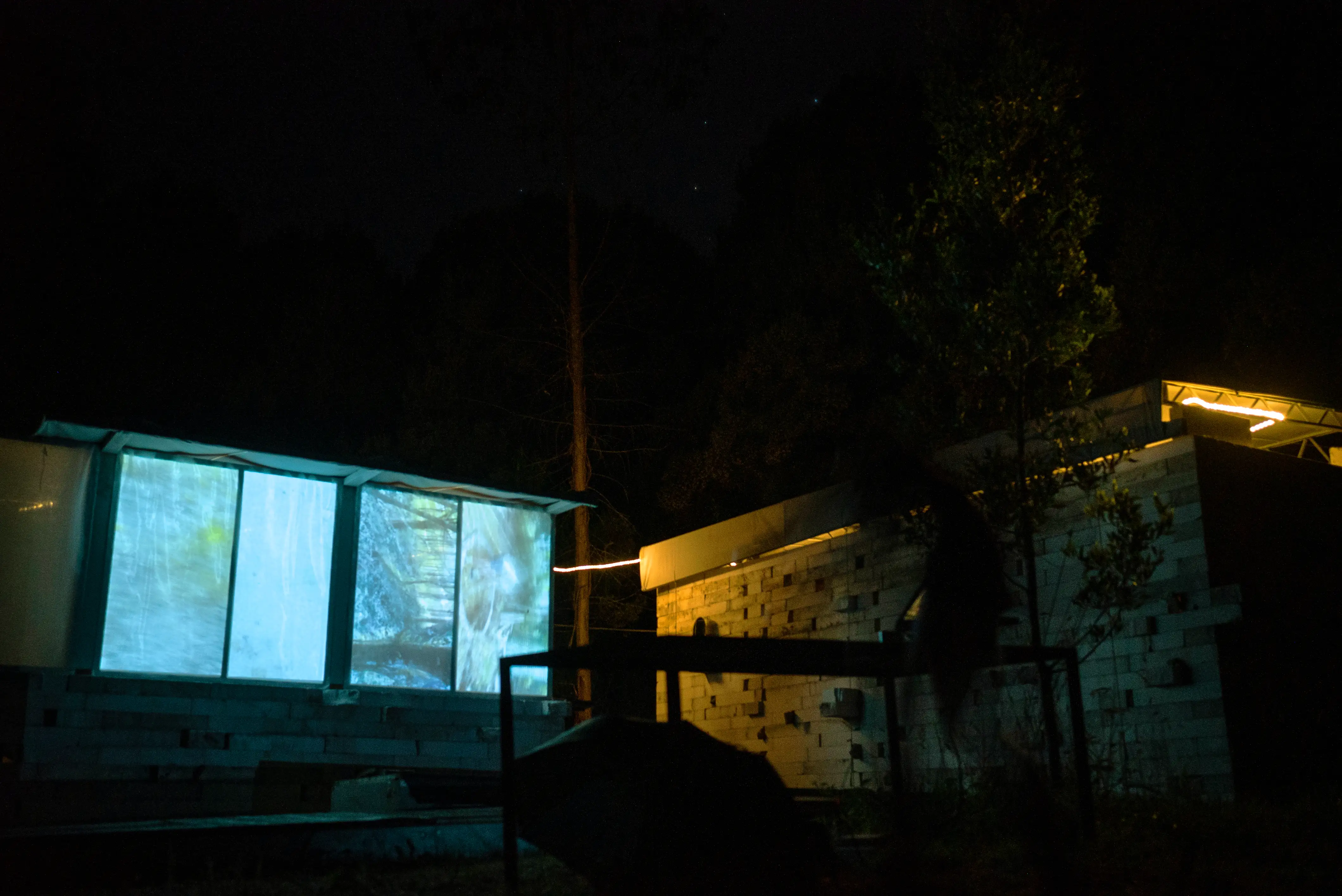 Four panels of phone footage are projected outside, side by side onto the side of a building at night.