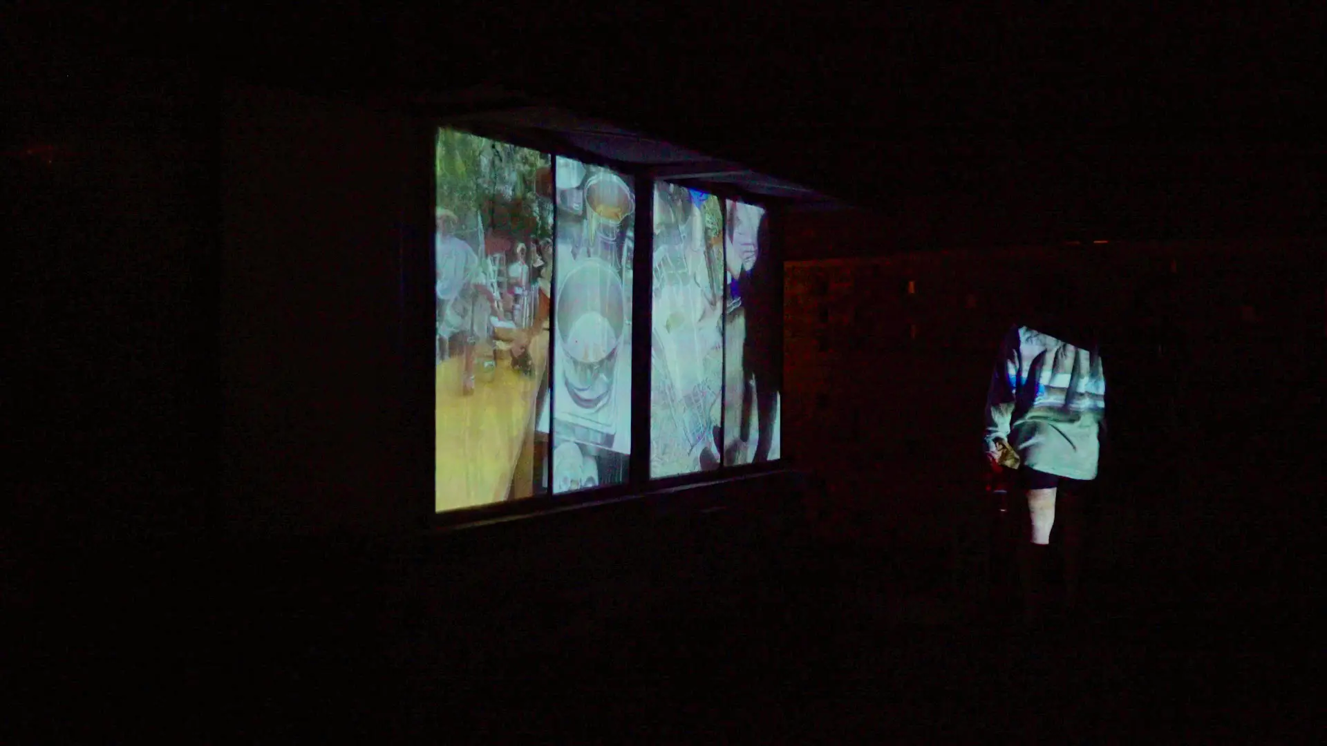 Someone stands in front of the projecting, blocking part of one of the four moving images.