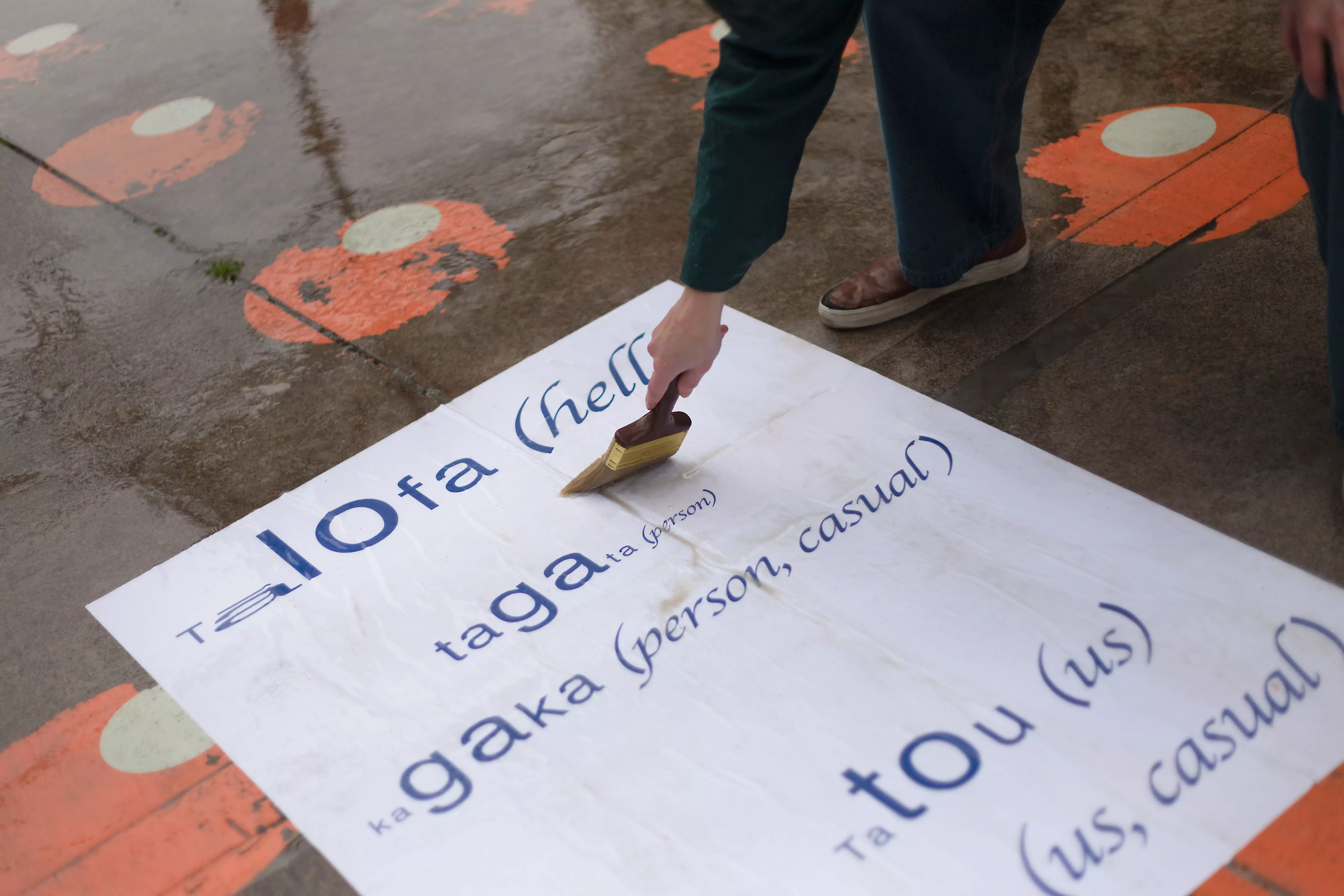 A poster being installed on the ground depicting Samoan pronunciation concrete poetry.