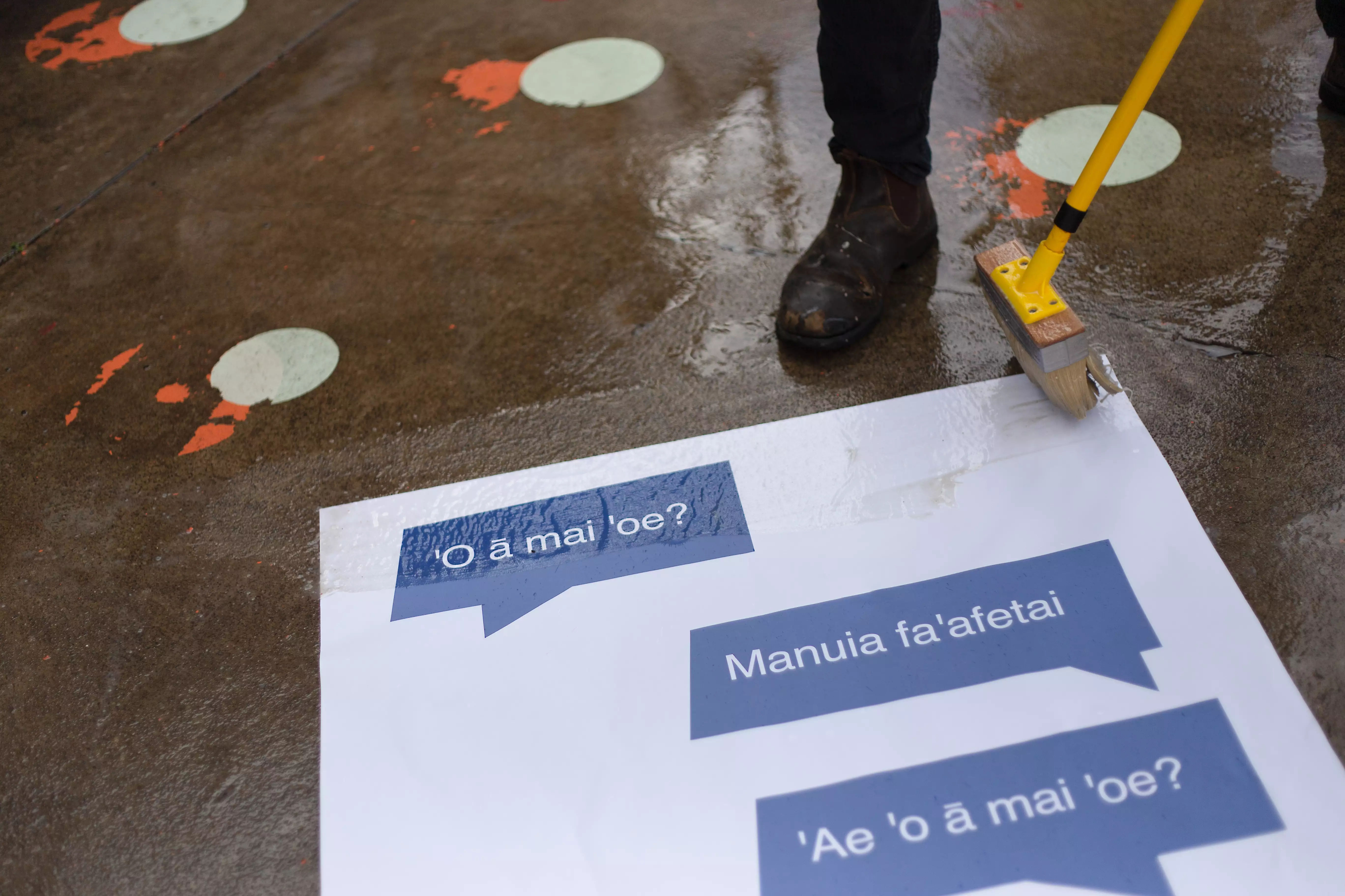 A poster being installed on the ground depicting basic Samoan phrases.