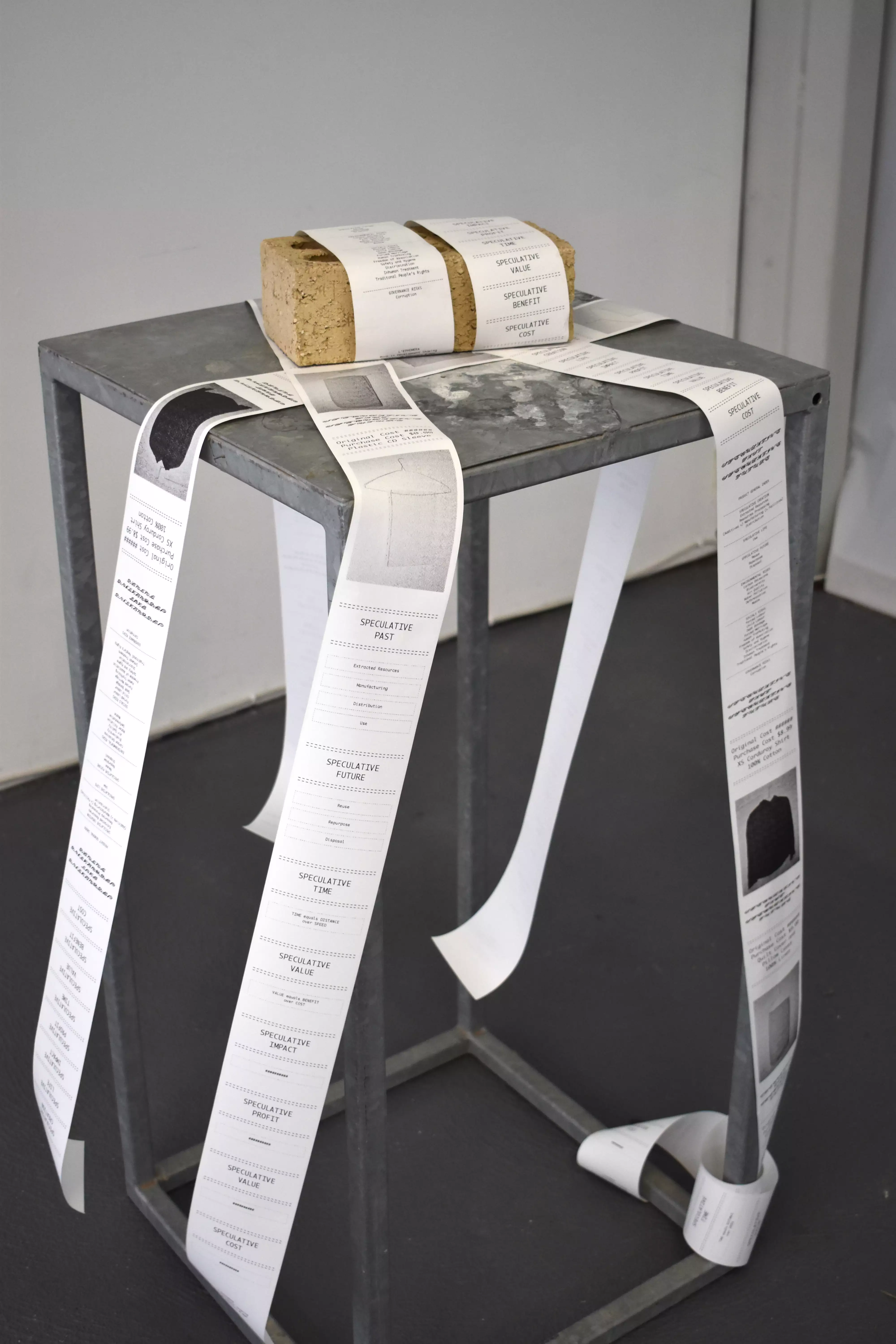 Long receipts containing research are weighed down by a brick on top of a grey metal plinth.